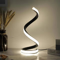 Helix Glow Table Lamp lit on a bedside table, warm light tracing its curved form